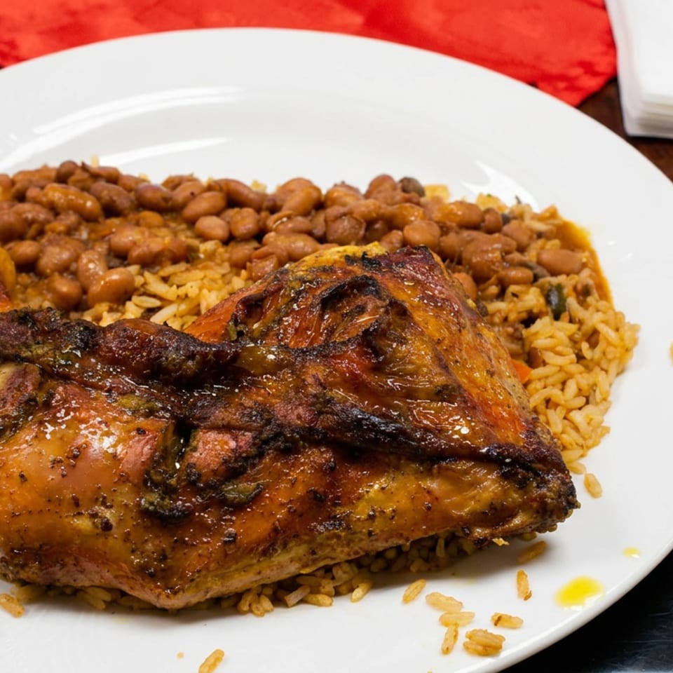 Roasted chicken leg served over seasoned rice and beans on a white plate at a restaurant table.