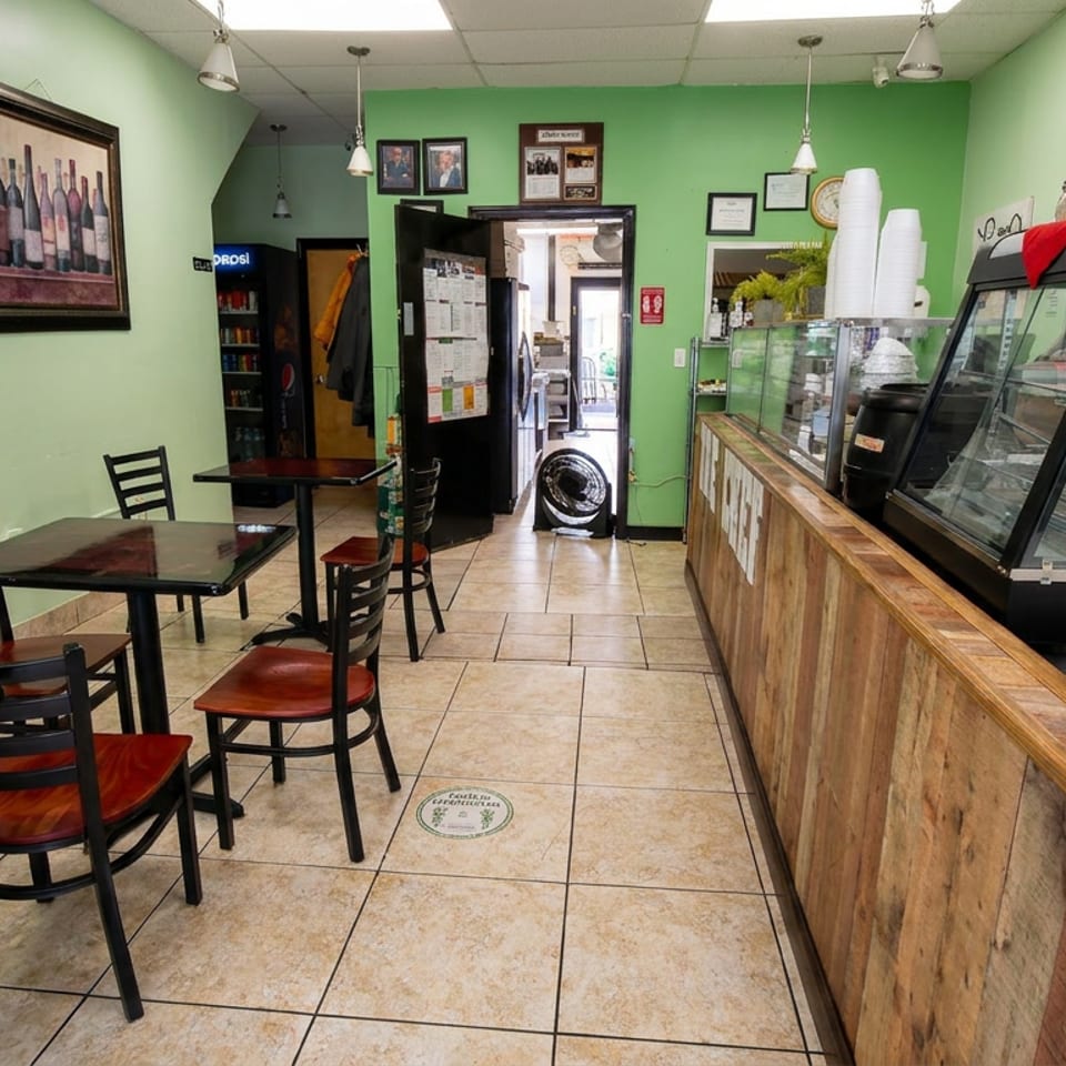 Green-walled restaurant interior with red-cushioned tables, framed artwork, tiled floor, and a wooden counter with glass food display cases.