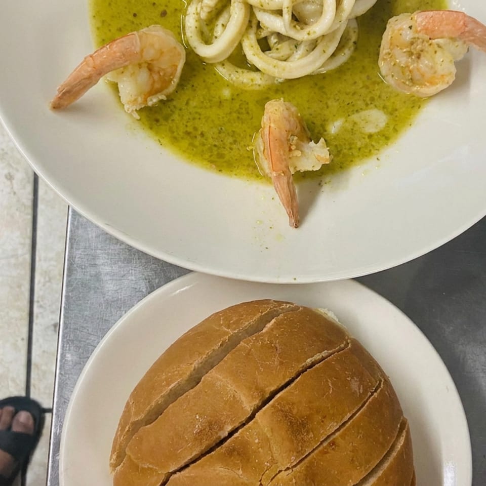 Plate of shrimp and pasta in green sauce beside sliced bread on a restaurant table.