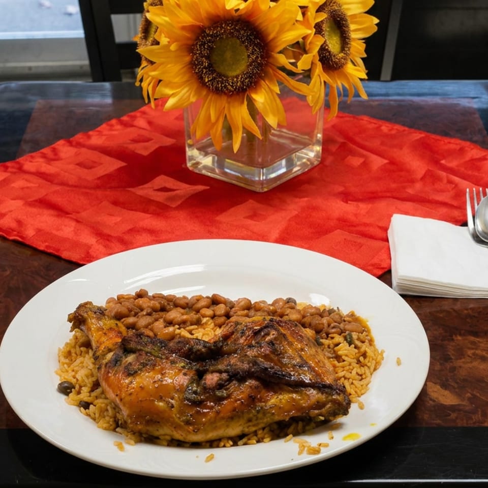 Grilled chicken served over yellow rice and beans on a white plate, with sunflowers, red table runner, and silverware.
